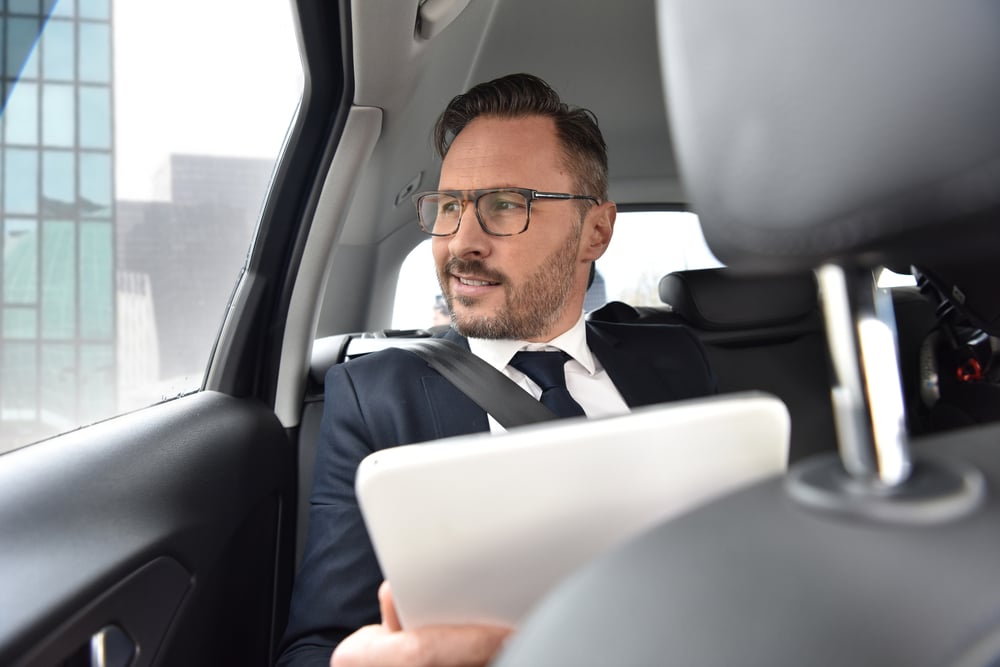 Businessman in taxi cab reading new on digital tablet