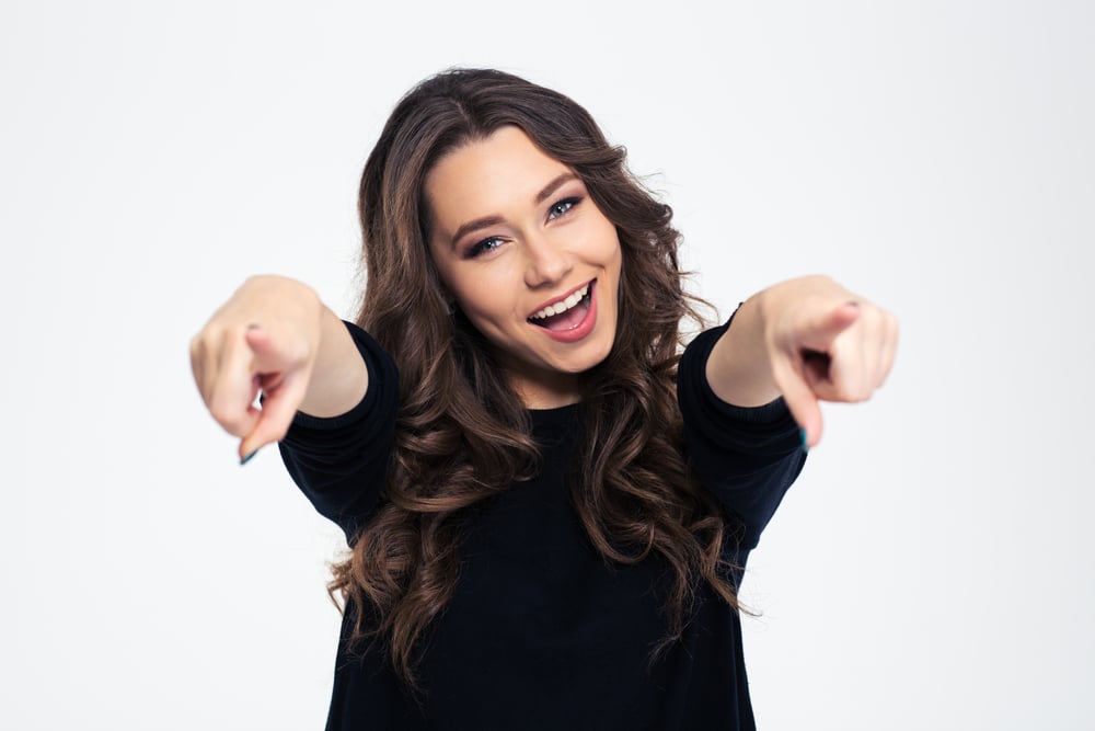 Portrait of a cheerful woman pointing at camera isolated on a white background