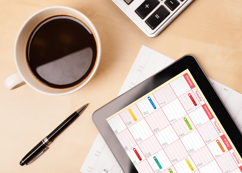 Workplace with tablet pc showing calendar and a cup of coffee on a wooden work table close-up