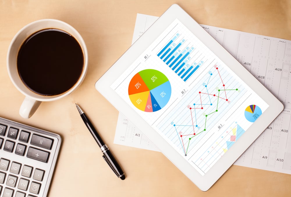 Workplace with tablet pc showing charts and a cup of coffee on a wooden work table close-up-1